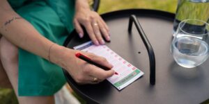 LOTO 5 Z 35 Na obrázku sa nachádza žena v zelených šatách, ktorá má na čiernom stolíku položený LOTO 5 z 35 tiket. Vypisuje svoje výherné čísla.