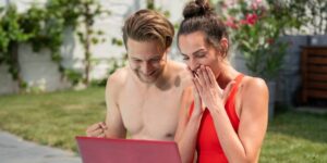 Na obrazku sa nachadza mlady muz a mlada zena. Sedia pri bazene a pozeraju sa do obrazovky notebooku. Tesia sa z vyhry v LOTO.